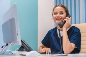 Smiling,Young,Woman,Nurse,Receptionist,Talking,On,Phone,While,Working